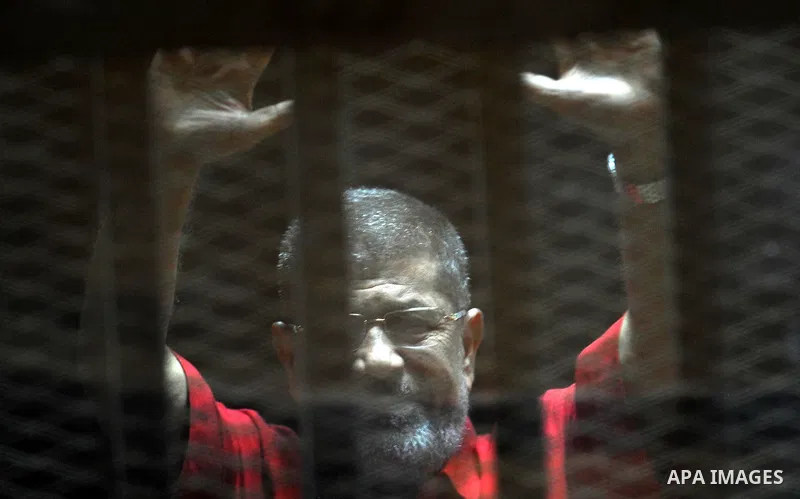 Ousted Egyptian president Mohammed Morsi waves as he stands behind bars during his trail in a court in Cairo on August 8, 2015. Cairo Criminal Court resumes on Saturday the trial of former Islamist president Mohamed Mors...