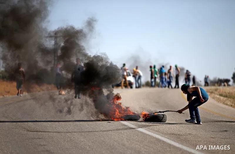 A Palestinian protester burns tires during clashes with Israeli security forces on a street leading to Duma village, in a demonstration following the funeral of Saad Dawabsha, the father of a Palestinian toddler killed l...