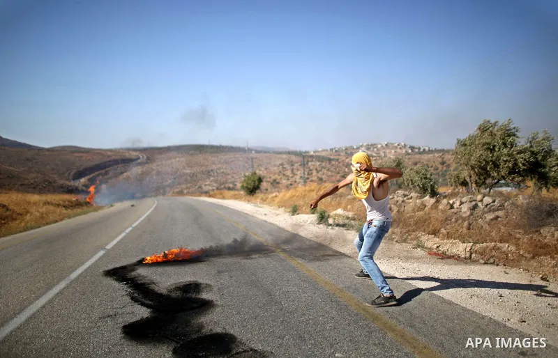 A Palestinian protester throws stones towards Israeli security forces during clashes on a street leading to Duma village, in a demonstration following the funeral of Saad Dawabsha, the father of a Palestinian toddler kil...