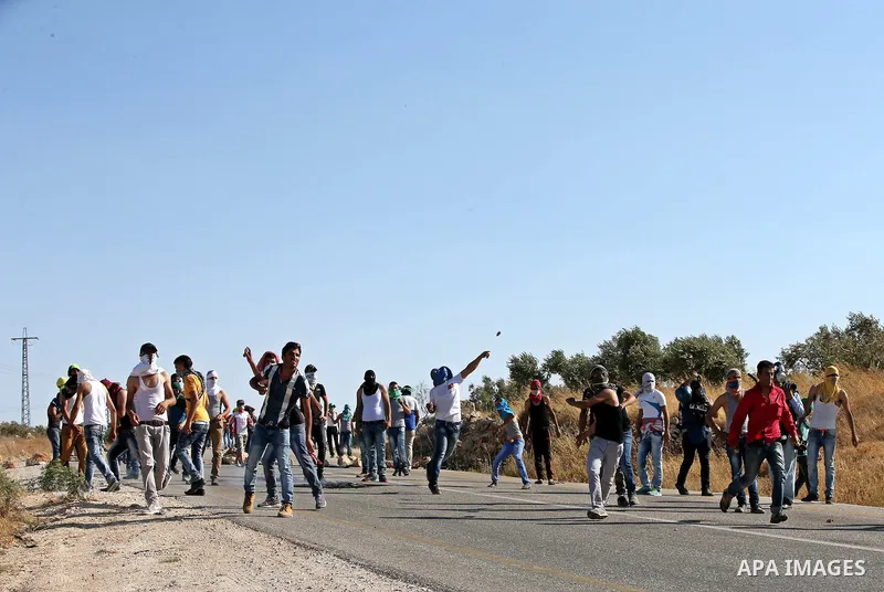 Palestinian protesters throw stones towards Israeli security forces during clashes on a street leading to Duma village, in a demonstration following the funeral of Saad Dawabsha, the father of a Palestinian toddler kille...