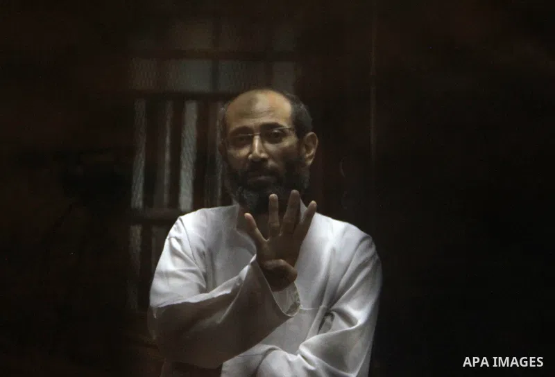 An Egyptian Muslim Brotherhood defendant waves as he stands behind the bars during his trial, along with ousted Islamist president Mohamed Morsi (unseen), in a court in Cairo on August 9, 2015. Cairo Criminal Court resum...