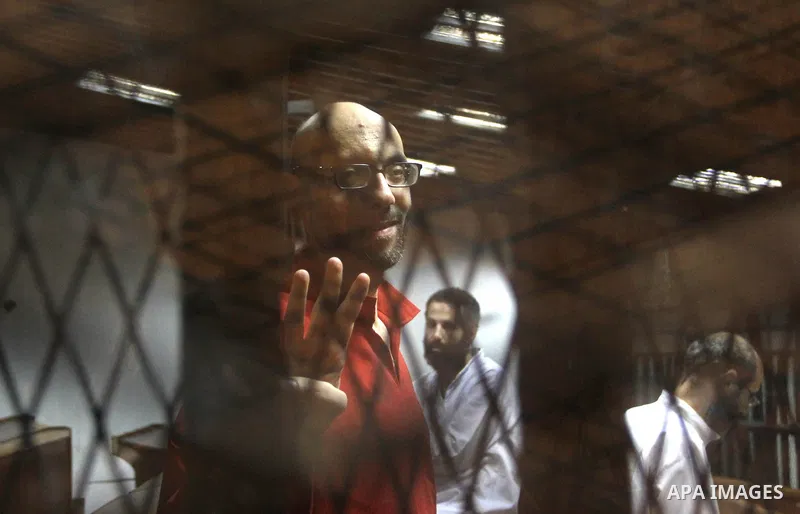 An Egyptian Muslim Brotherhood defendant waves as he stands behind the bars during his trial, along with ousted Islamist president Mohamed Morsi (unseen), in a court in Cairo on August 9, 2015. Cairo Criminal Court resum...