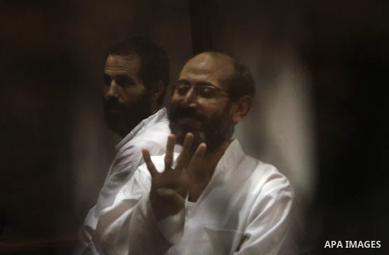 An Egyptian Muslim Brotherhood defendant waves as he stands behind the bars during his trial, along with ousted Islamist president Mohamed Morsi (unseen), in a court in Cairo on August 9, 2015. Cairo Criminal Court resum...