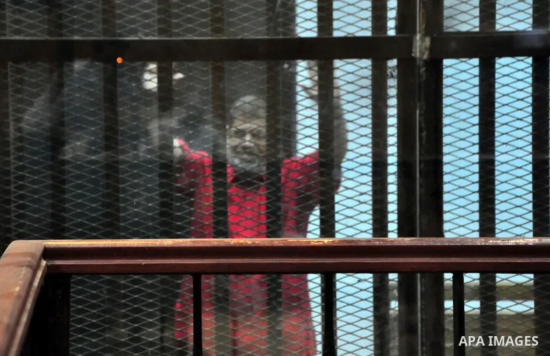 Ousted Egyptian president Mohammed Morsi waves as he stands behind bars during his trail in a court in Cairo on August 10, 2015. The Cairo court resumed hearing evidence in the so-called Qatar espionage trial of Morsi, a...