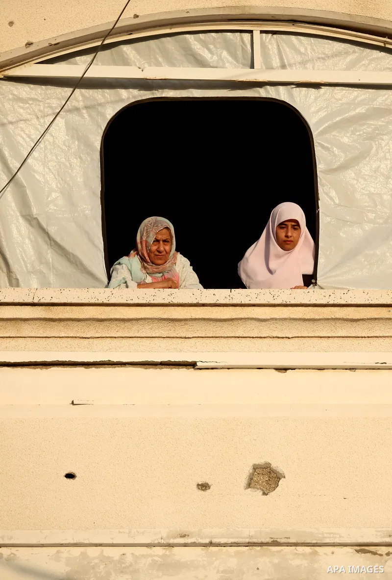 Palestinians look on from their destroyed house as members of Ezzedeen al-Qassam brigades, the armed wing of Hamas movement, take part in an anti-Israel parade in Beit Hanoun, in the northern Gaza Strip, on August 11, 20...