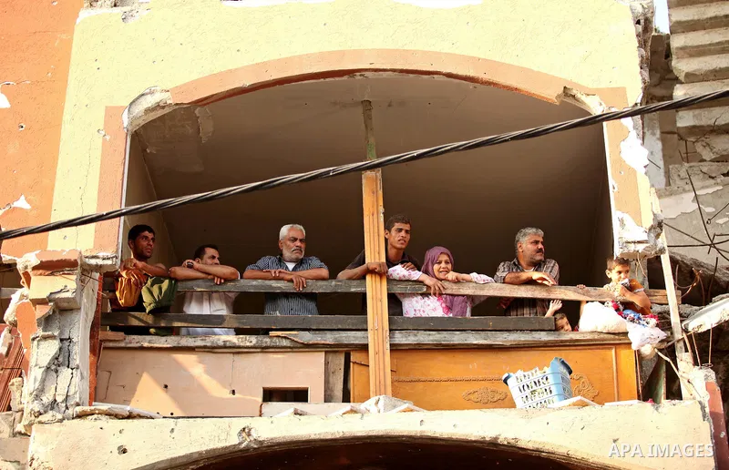 Palestinians look on from their destroyed house as members of Ezzedeen al-Qassam brigades, the armed wing of Hamas movement, take part in an anti-Israel parade in Beit Hanoun, in the northern Gaza Strip, on August 11, 20...