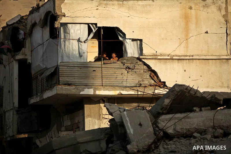 Palestinians look from destroyed house as members of Ezzedeen al-Qassam brigades, the armed wing of Hamas movement, take part in an anti-Israel parade in Beit Hanoun, in the northern Gaza Strip, on August 11, 2015. Photo...
