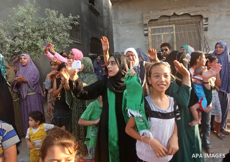 Palestinians look on as members of Ezzedeen al-Qassam brigades, the armed wing of Hamas movement, take part in an anti-Israel parade in Beit Hanoun, in the northern Gaza Strip, on August 11, 2015. Photo by Ashraf Amra