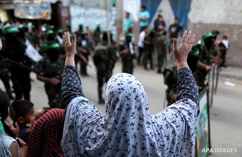 Palestinians look on as members of Ezzedeen al-Qassam brigades, the armed wing of Hamas movement, take part in an anti-Israel parade in Beit Hanoun, in the northern Gaza Strip, on August 11, 2015. Photo by Ashraf Amra