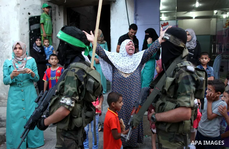 Palestinians look on as members of Ezzedeen al-Qassam brigades, the armed wing of Hamas movement, take part in an anti-Israel parade in Beit Hanoun, in the northern Gaza Strip, on August 11, 2015. Photo by Ashraf Amra