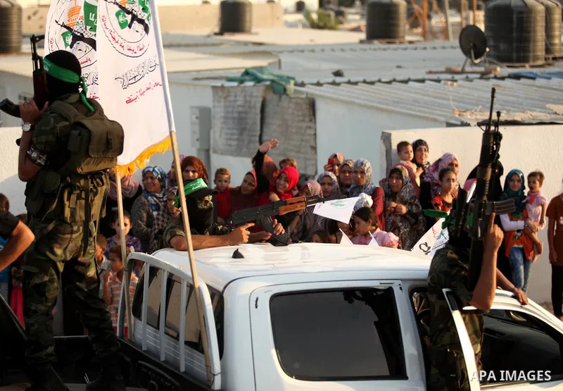 Palestinians look on as members of Ezzedeen al-Qassam brigades, the armed wing of Hamas movement, take part in an anti-Israel parade in Beit Hanoun, in the northern Gaza Strip, on August 11, 2015. Photo by Ashraf Amra