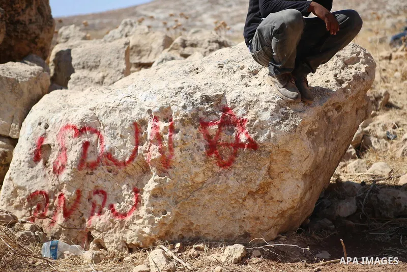 A Palestinian man sits on the rock graffiti written in Hebrew in the area of Ein Samiya near Kafr Malik village in northern Ramallah, on August, 13, 2015. A group of Israeli settlers raided the village of Ein Samiya and...