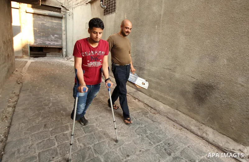 Nour, a 18-year-old Syrian man, walks with his relative in a rebel-controlled area of Aleppo, on August 13, 2015. Nour lost his leg following a bomb barrel attack by forces of Syria's President Bashar al-Assad near his h...