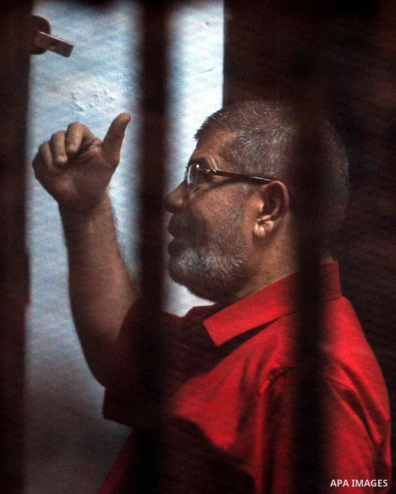 Ousted Egyptian president Mohammed Morsi waves as he stands behind bars during his trail in a court in Cairo on August 16, 2015. Cairo criminal court resumes today, Sunday, the trial of deposed president Mohamed Morsi an...