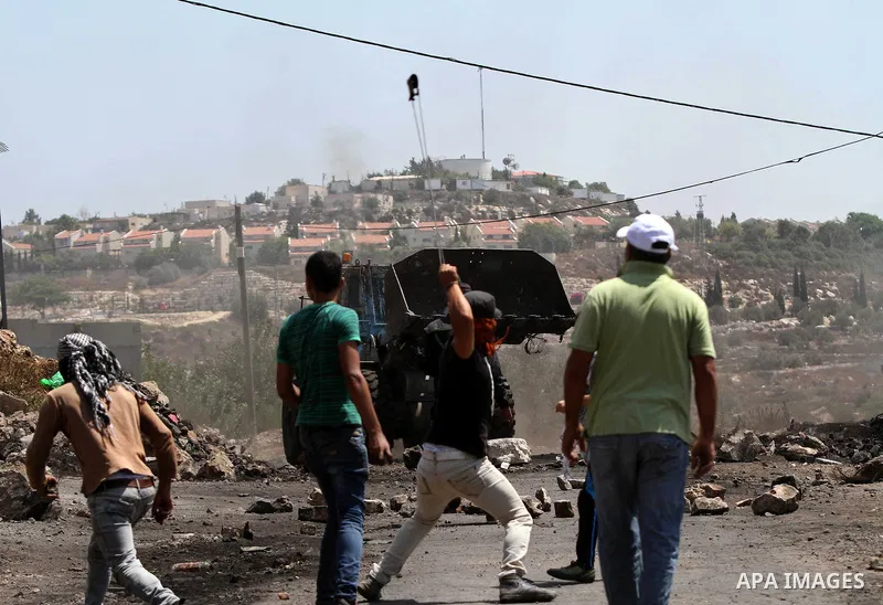 A Palestinian protester uses a slingshot to throw a stone towards an Israeli military bulldozer during clashes following a demonstration against the expropriation of Palestinian land by Israel in the village of Kfar Qadd...