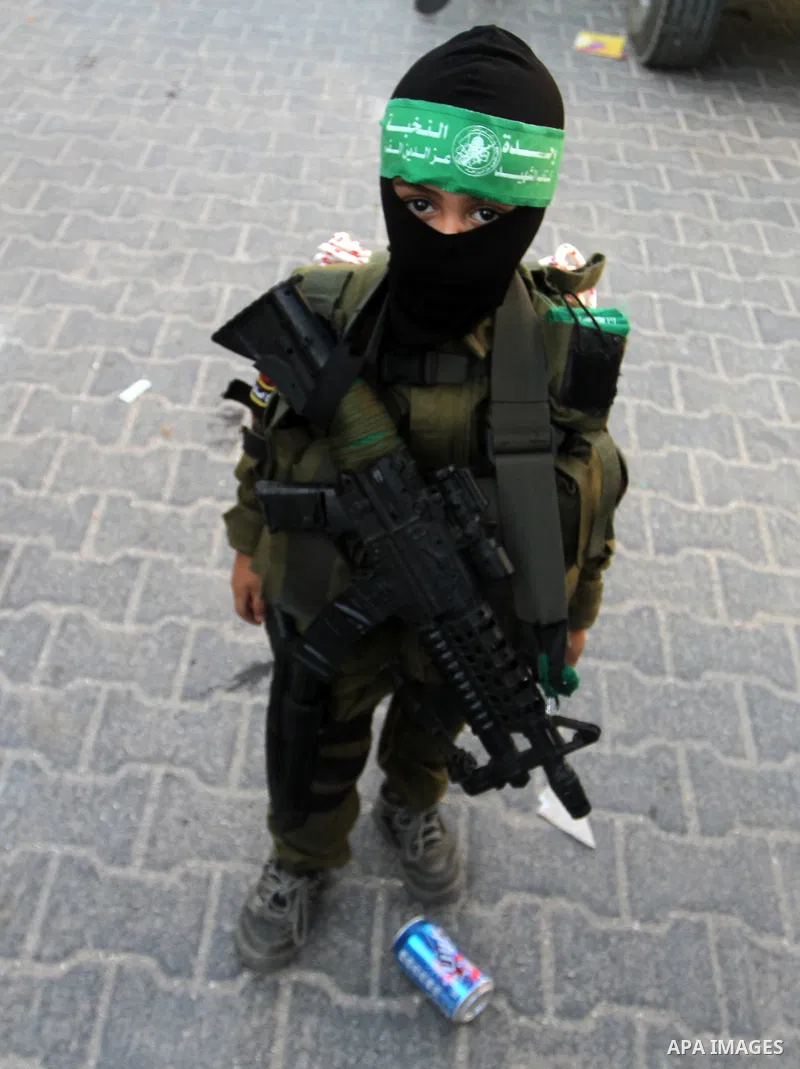 A Palestinian boy wears the al-Qassam Brigades costume during a military parade marking the first anniversary of the killing of Hamas's military commanders Mohammed Abu Shamala and Raed al-Attar, in Rafah in the southern...
