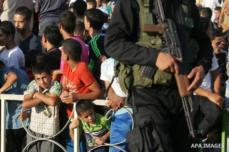 Palestinian children watch a military parade of members of the al-Qassam Brigades, the armed wing of the Hamas movement, to mark the first anniversary of the killing of Hamas's military commanders Mohammed Abu Shamala an...