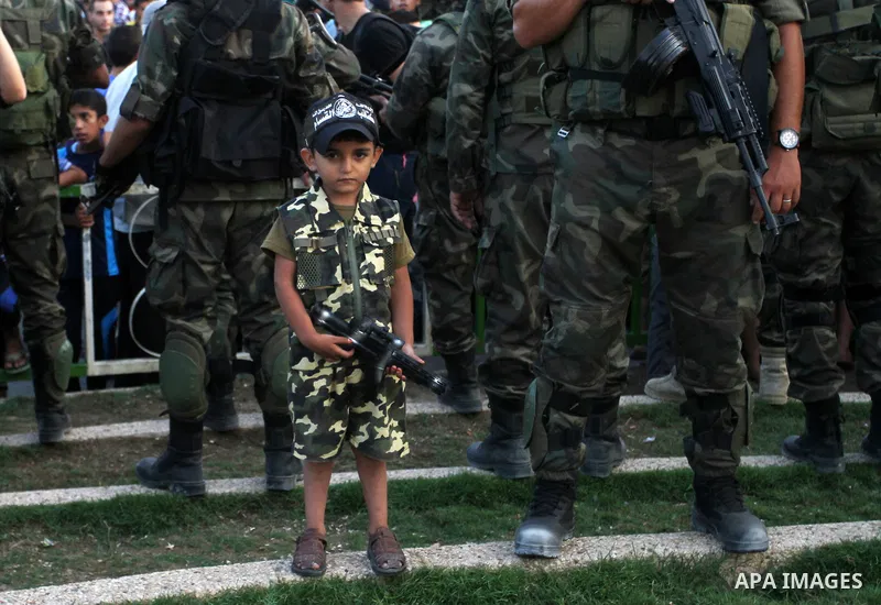 A Palestinian boy wears the al-Qassam Brigades costume during a military parade marking the first anniversary of the killing of Hamas's military commanders Mohammed Abu Shamala and Raed al-Attar, in Rafah in the southern...