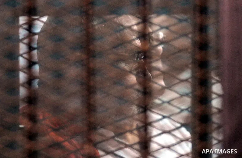 Egyptian Muslim Brotherhood leader Mohamed Badie sits behind the defendant's cage as he attends his trial, in a courtroom in Torah prison, southern Cairo, Egypt, Saturday, Aug. 22, 2015. The court sentenced Muslim Brothe...