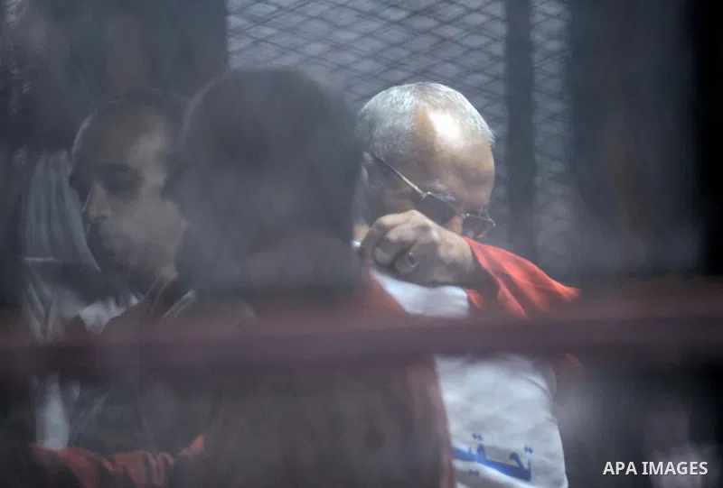 Egyptian Muslim Brotherhood leader Mohamed Badie sits behind the defendant's cage as he attends his trial, in a courtroom in Torah prison, southern Cairo, Egypt, Saturday, Aug. 22, 2015. The court sentenced Muslim Brothe...