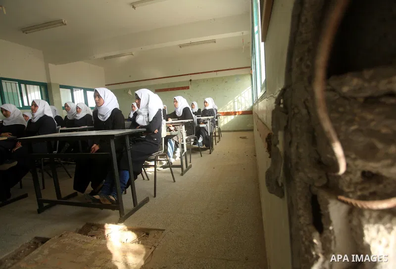 Palestinian schoolgirls, pictured through a hole in the roof of a classroom that witnesses said was damaged by Israeli shelling during a 50-day war last summer, attend a lesson on the first day of a new school year at Su...