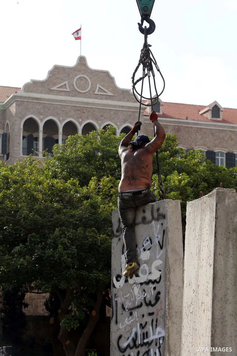 Municipality employees dismantle a concrete blast wall spread with graffiti depicting various political groups and bearing messages against police brutality in front of the seat of the government in central Beirut, on Au...