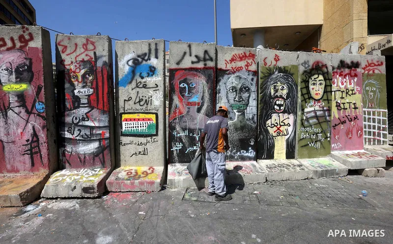 A Lebanese worker collects garbage in front of a concrete blast wall, spread with graffiti depicting various political groups and bearing messages against police brutality, before its dismantlement, in front of the seat...
