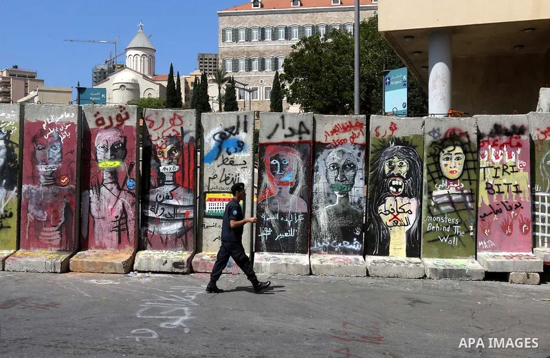 A Lebanese policeman walks past a concrete blast wall, spread with graffiti depicting various political groups and bearing messages against police brutality, before its dismantlement, in front of the seat of the governme...