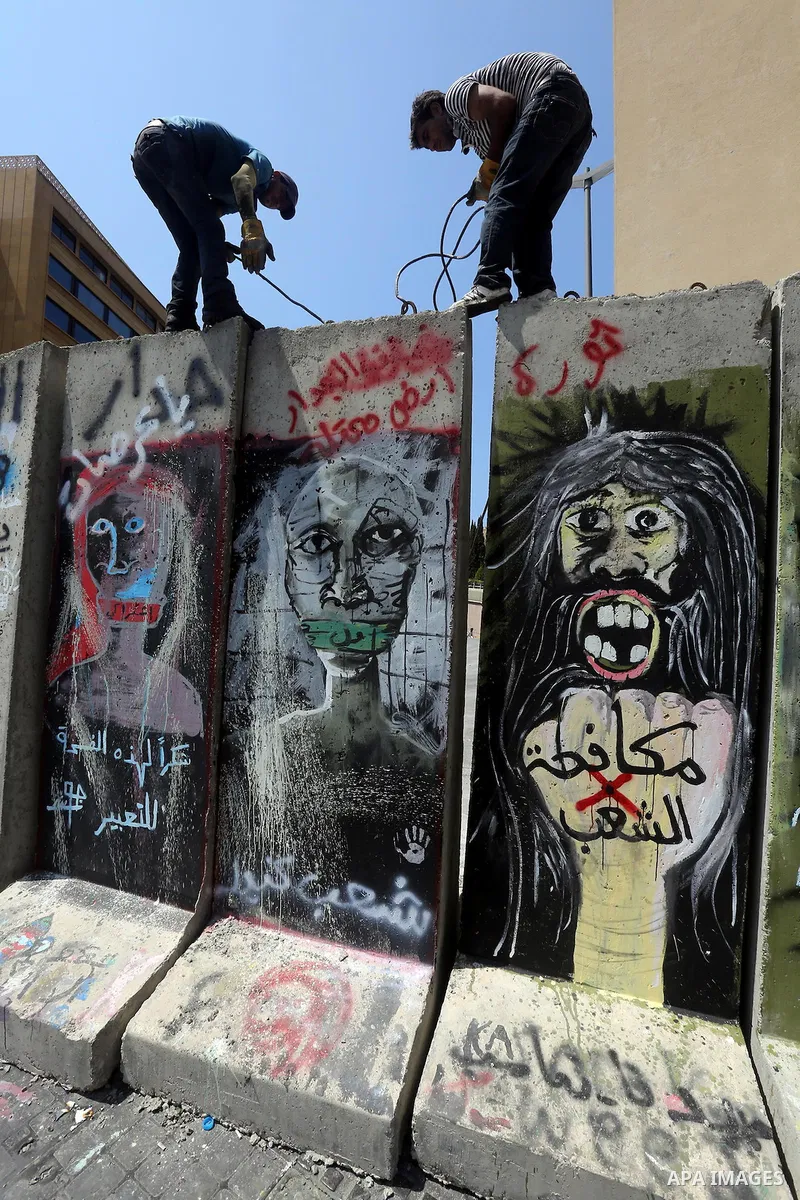 Municipality employees dismantle a concrete blast wall spread with graffiti depicting various political groups and bearing messages against police brutality in front of the seat of the government in central Beirut, on Au...