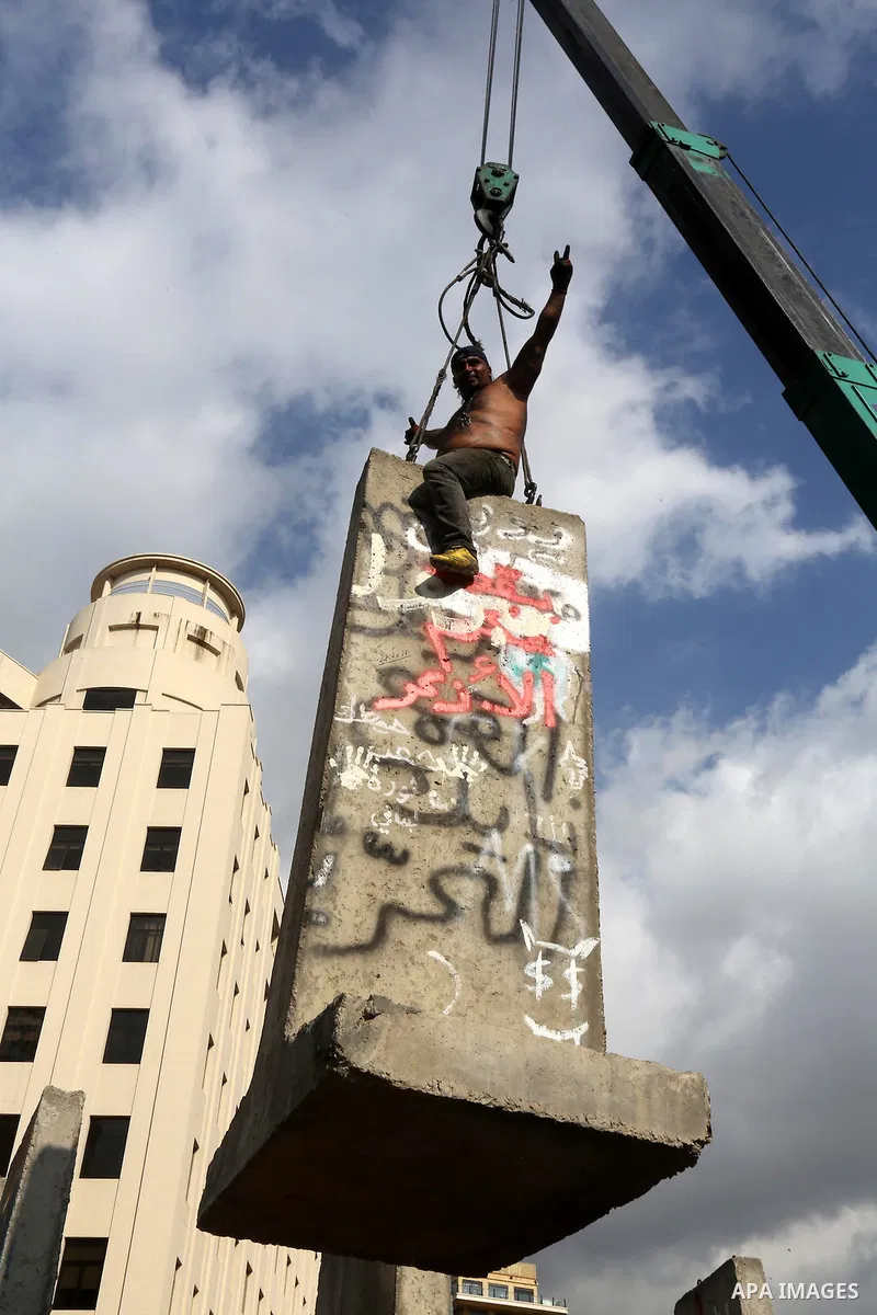Municipality employees dismantle a concrete blast wall spread with graffiti depicting various political groups and bearing messages against police brutality in front of the seat of the government in central Beirut, on Au...