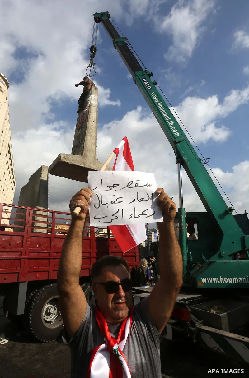 A Lebanese protester holds a placard as municipality employees dismantle a concrete blast wall spread with graffiti depicting various political groups and bearing messages against police brutality in front of the seat of...
