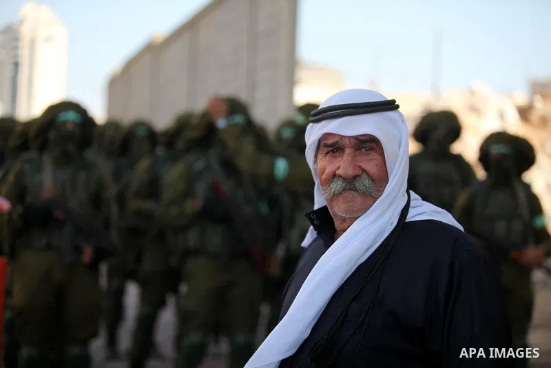 A Palestinian man looks on in front of militants of the Ezzedine al-Qassam Brigades, Hamas' armed wing, during a military parade in Gaza city on August 26, 2015. Photo by Ashraf Amra