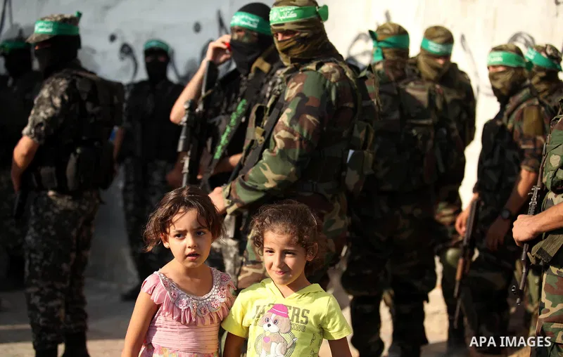 Palestinian girls stand in front of militants of the Ezzedine al-Qassam Brigades, Hamas' armed wing, during a military parade in Gaza city on August 26, 2015. Photo by Ashraf Amra