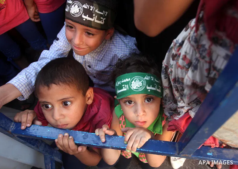 Palestinian children look on as militants of the Ezzedine al-Qassam Brigades, Hamas' armed wing, take part in a military parade in Gaza city on August 26, 2015. Photo by Ashraf Amra