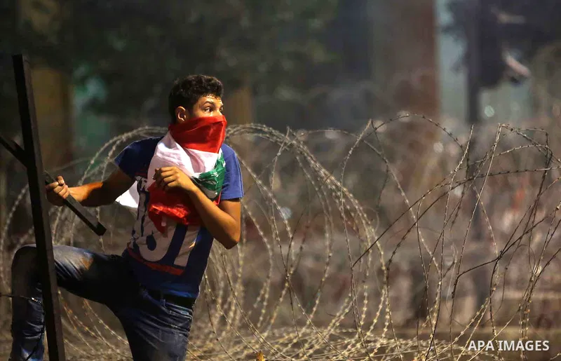 Protesters carry banners and Lebanese national flags as they stand near barbed wire erected near the government palace in downtown Beirut, Lebanon August 29, 2015. Thousands of protesters waving Lebanese flags and chanti...