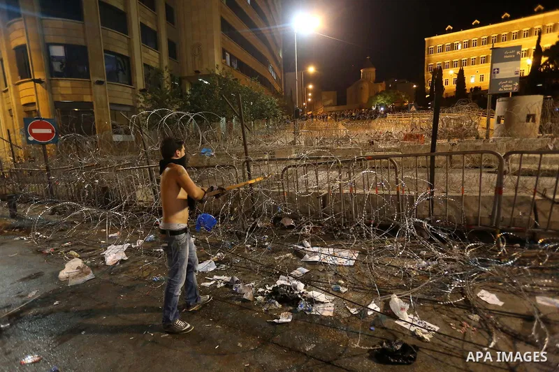 Protesters carry banners and Lebanese national flags as they stand near barbed wire erected near the government palace in downtown Beirut, Lebanon August 29, 2015. Thousands of protesters waving Lebanese flags and chanti...