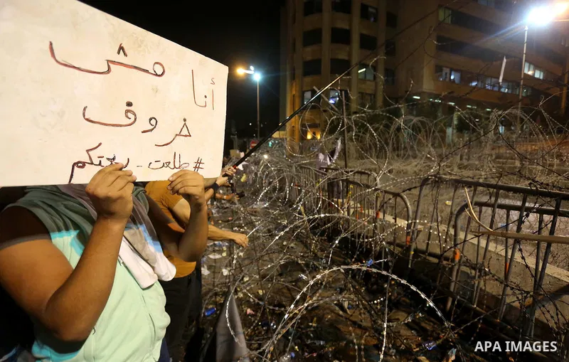 Protesters carry banners and Lebanese national flags as they stand near barbed wire erected near the government palace in downtown Beirut, Lebanon August 29, 2015. Thousands of protesters waving Lebanese flags and chanti...