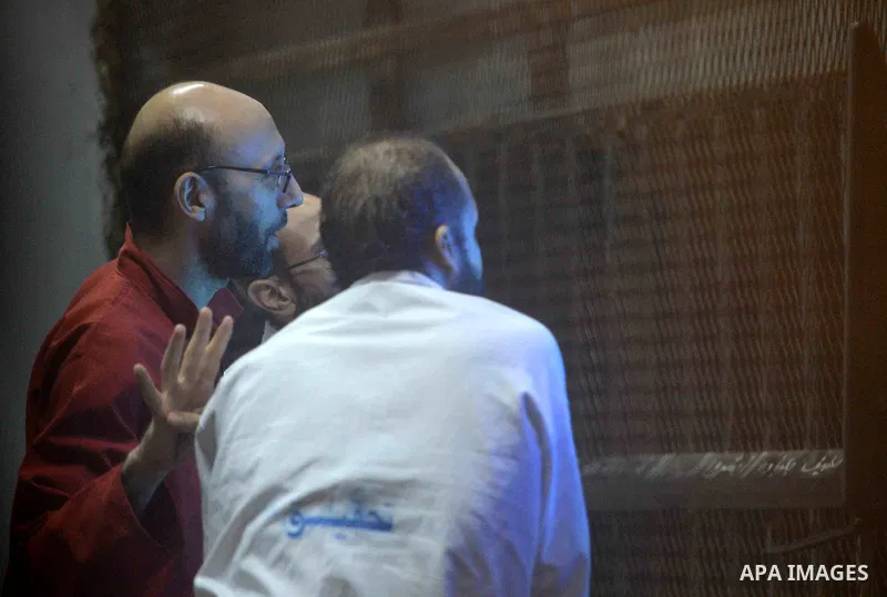 Egyptian Muslim Brotherhood defendants wave as they stand behind the bars during their trial, along with ousted Islamist president Mohamed Morsi (unseen) in Cairo on August 30, 2015. Cairo criminal court resumes today th...