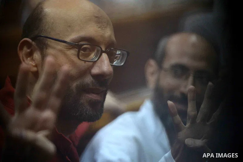 Egyptian Muslim Brotherhood defendants wave as they stand behind the bars during their trial, along with ousted Islamist president Mohamed Morsi (unseen) in Cairo on August 30, 2015. Cairo criminal court resumes today th...