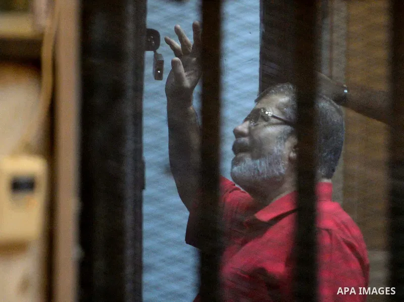 Ousted Egyptian president Mohammed Morsi waves as he stands behind bars during his trail in a court in Cairo on August 30, 2015. Cairo criminal court resumes today the trial of deposed president Mohamed Morsi and 10 othe...