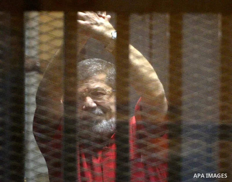 Ousted Egyptian president Mohammed Morsi waves as he stands behind bars during his trail in a court in Cairo on August 30, 2015. Cairo criminal court resumes today the trial of deposed president Mohamed Morsi and 10 othe...