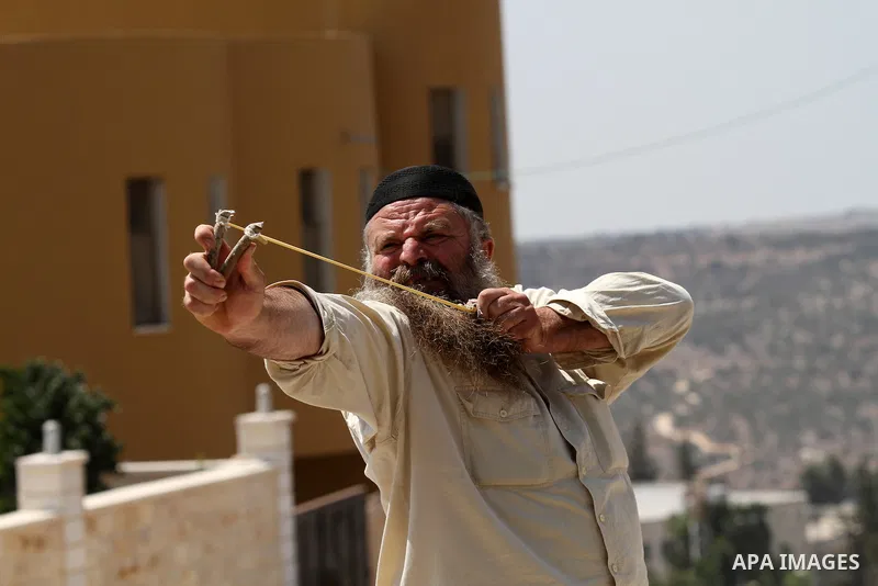 A Palestinian man uses a slingshot to throw stones towards Israeli security forces during clashes following a demonstration against the expropriation of Palestinian land by Israel, in the village of Kfar Qaddum, near Nab...