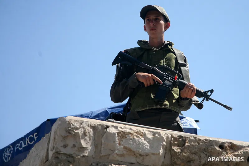 An Israeli policeman stands guard as Palestinian Muslim worshippers, under the age of 40 years old, perform the traditional Friday prayers on a street, outside the Old City walls in East Jerusalem on September 18, 2015....