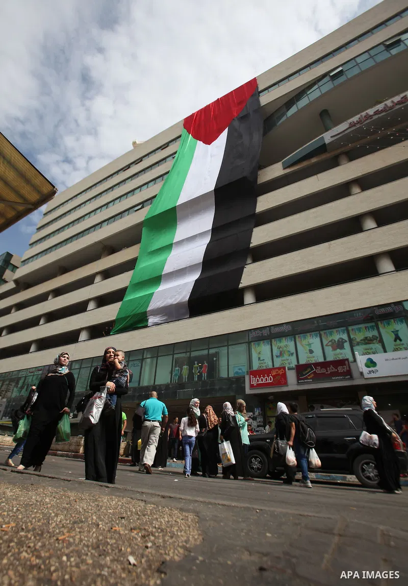 Palestinians walk past their national flag hanged on a building during an event to support Palestinian President Mahmoud Abbas in the West Bank city of Nablus on September 30, 2015. Abbas has circulated a hard-hitting cr...