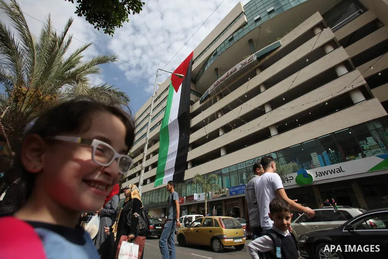 Palestinians walk past their national flag hanged on a building during an event to support Palestinian President Mahmoud Abbas in the West Bank city of Nablus on September 30, 2015. Abbas has circulated a hard-hitting cr...