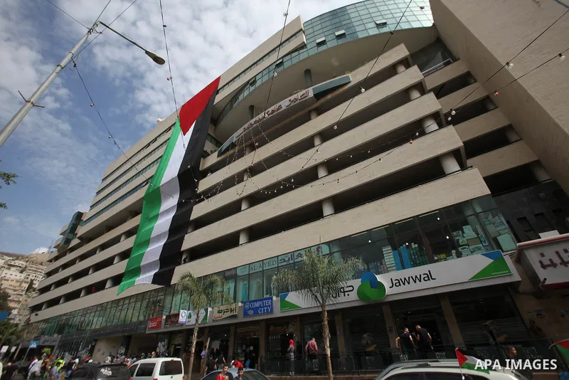Palestinians walk past their national flag hanged on a building during an event to support Palestinian President Mahmoud Abbas in the West Bank city of Nablus on September 30, 2015. Abbas has circulated a hard-hitting cr...