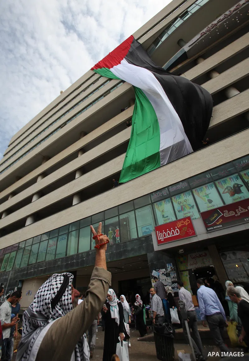 A Palestinian man flashes victory sign as he walks past his national flag hanged on a building during an event to support Palestinian President Mahmoud Abbas in the West Bank city of Nablus on September 30, 2015. Abbas h...