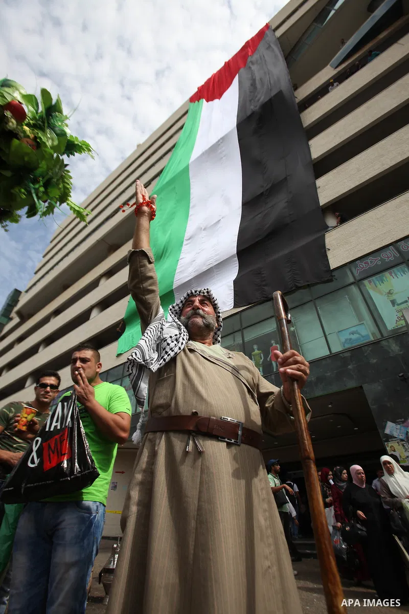 A Palestinian man flashes victory sign as he walks past his national flag hanged on a building during an event to support Palestinian President Mahmoud Abbas in the West Bank city of Nablus on September 30, 2015. Abbas h...