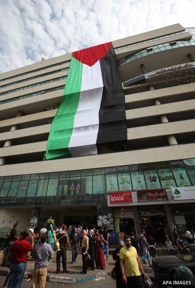 Palestinians walk past their national flag hanged on a building during an event to support Palestinian President Mahmoud Abbas in the West Bank city of Nablus on September 30, 2015. Abbas has circulated a hard-hitting cr...