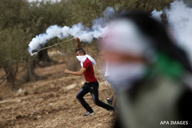 A Palestinian protester uses a sling shot to throw back a tear gas canister during clashes with Israeli security forces in Budrus village, west of Ramallah on October 2, 2015. Two Israeli settlers were shot and killed in...